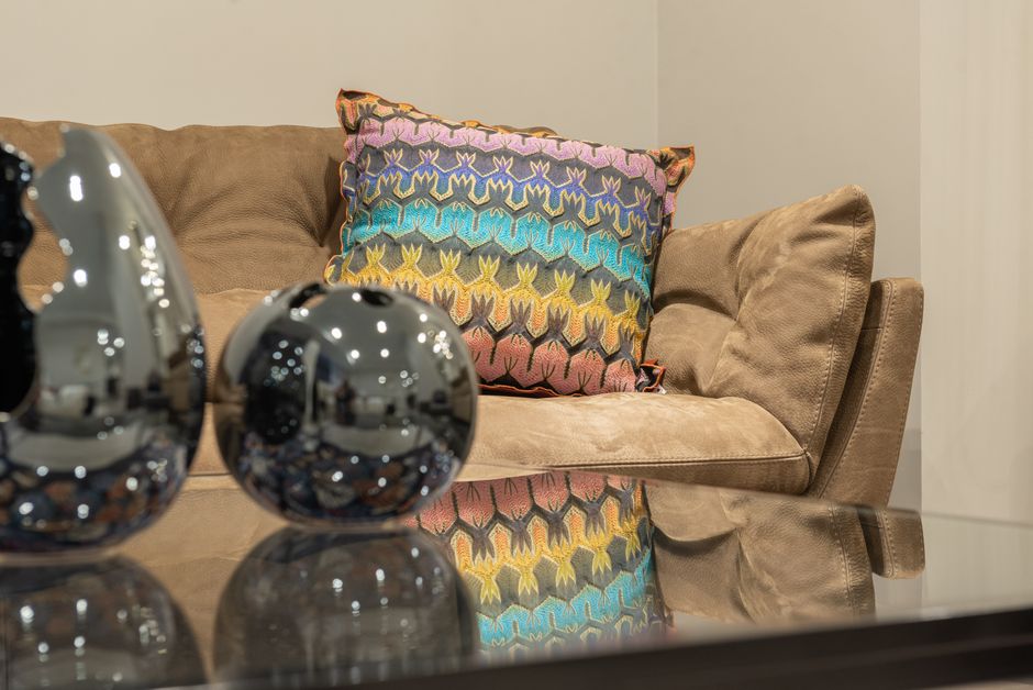 Modern living room interior with comfortable sofa and colorful cushion near table with glass tabletop and shiny decorations