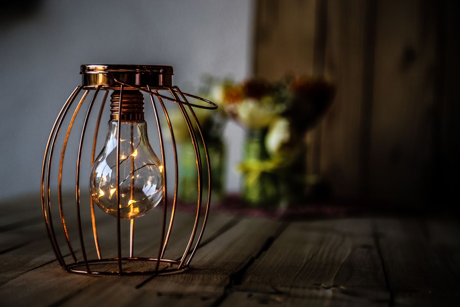 Warm, glowing light bulb in rustic metal cage on a wooden table, creating a cozy ambiance.